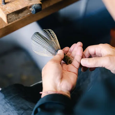 Hands holding a bamboo matcha whisk